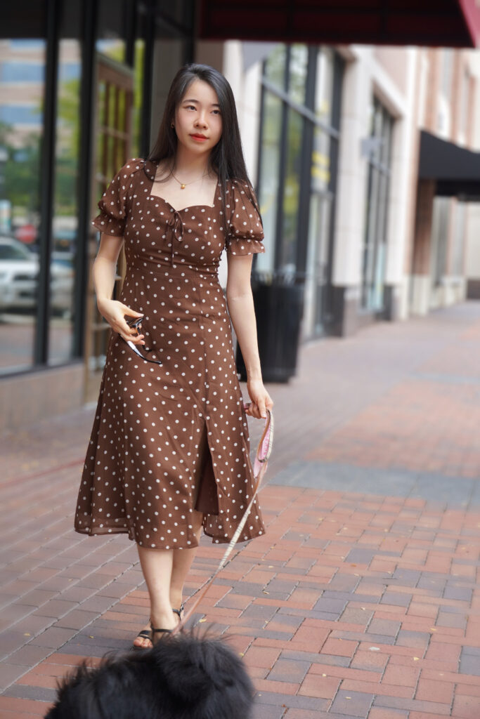 Vivian, a girl in brown polka dot dress, holds her pomeranian puppy with her lunch, salata salad