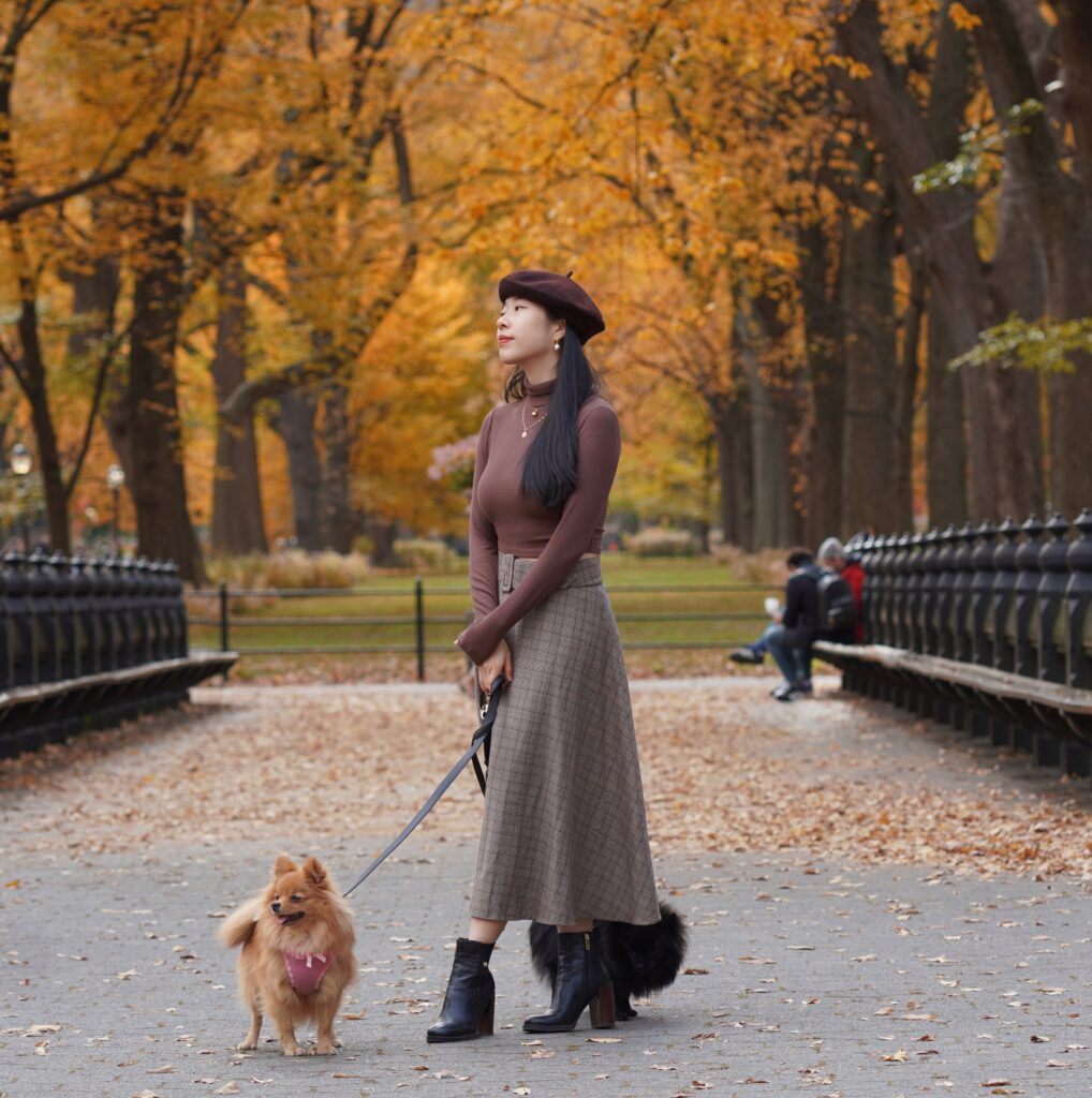 Vivian R Tang poses in dark academia preppy Tommy Hilfiger, Ralph Lauren plaid skirt / fashion in Central Park New York City NYC with her pomeranians against a fall setting