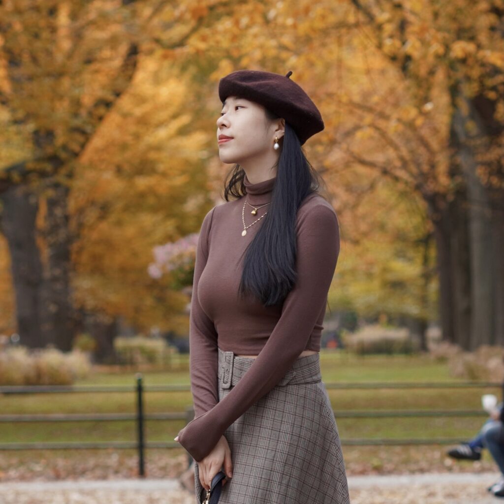 Vivian R Tang poses in dark academia preppy Tommy Hilfiger, Ralph Lauren plaid skirt / fashion in Central Park New York City NYC with her pomeranians against a fall setting